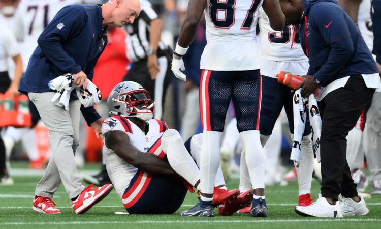 New England Patriots wide receiver A.J. Brown sits on the field as a trainer and teammates gather around him.
