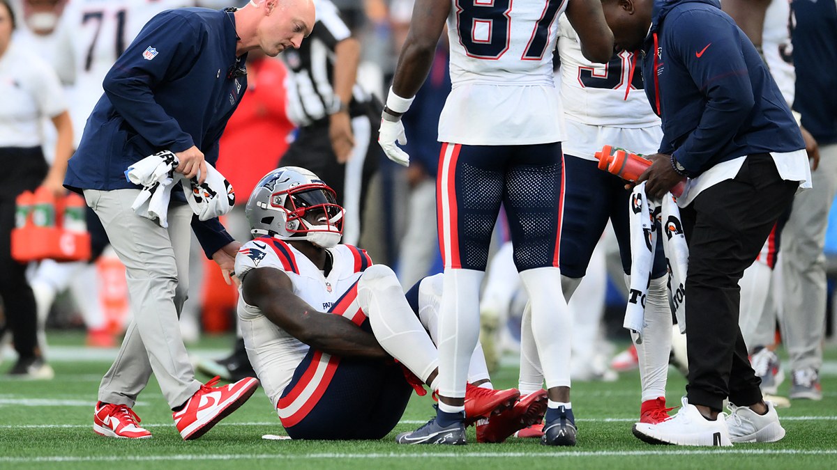 New England Patriots wide receiver A.J. Brown sits on the field as a trainer and teammates gather around him.