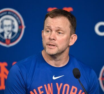 New York Mets manager Andrew Green speaks into a microphone during a press conference in front of a Mets backdrop.