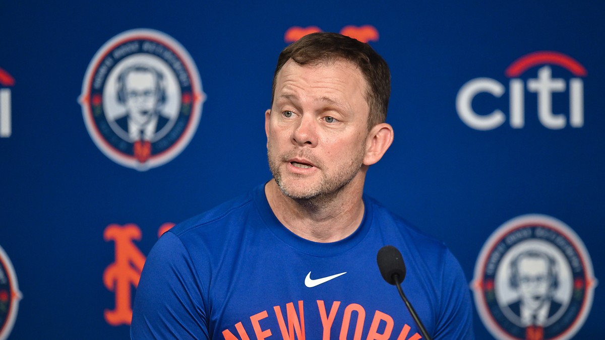 New York Mets manager Andrew Green speaks into a microphone during a press conference in front of a Mets backdrop.