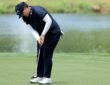 Golfer Angel Yin bends over her putter on the green with a pond behind her.