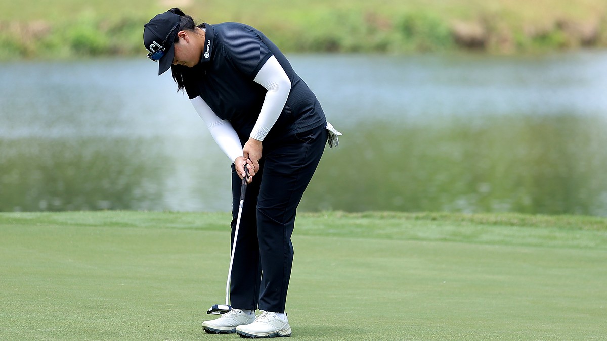 Golfer Angel Yin bends over her putter on the green with a pond behind her.