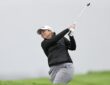 Golfer Angela Stanford follows through on an approach shot against a gray, overcast sky.