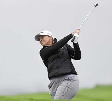 Golfer Angela Stanford follows through on an approach shot against a gray, overcast sky.