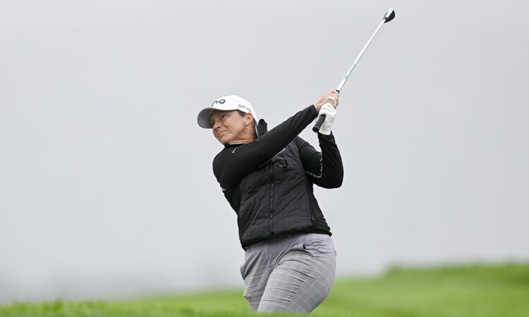 Golfer Angela Stanford follows through on an approach shot against a gray, overcast sky.