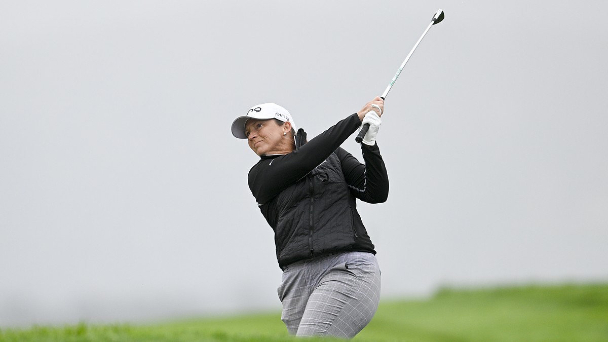 Golfer Angela Stanford follows through on an approach shot against a gray, overcast sky.