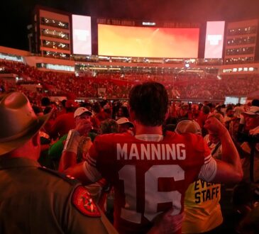 Texas quarterback Arch Manning stands with his back to the camera in his No. 16 jersey as fans flood the field around him.