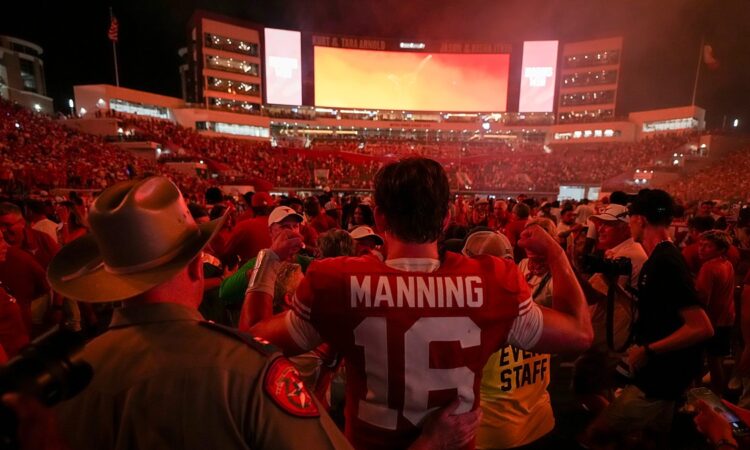 Texas quarterback Arch Manning stands with his back to the camera in his No. 16 jersey as fans flood the field around him.