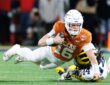 Texas Longhorns quarterback Arch Manning stretches the ball forward as Michigan's Jordan Young tackles him.