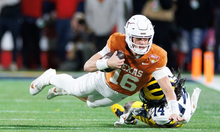 Texas Longhorns quarterback Arch Manning stretches the ball forward as Michigan's Jordan Young tackles him.