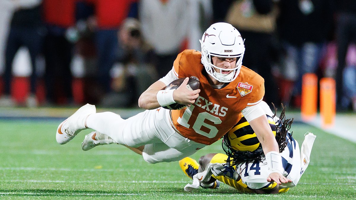 Texas Longhorns quarterback Arch Manning stretches the ball forward as Michigan's Jordan Young tackles him.