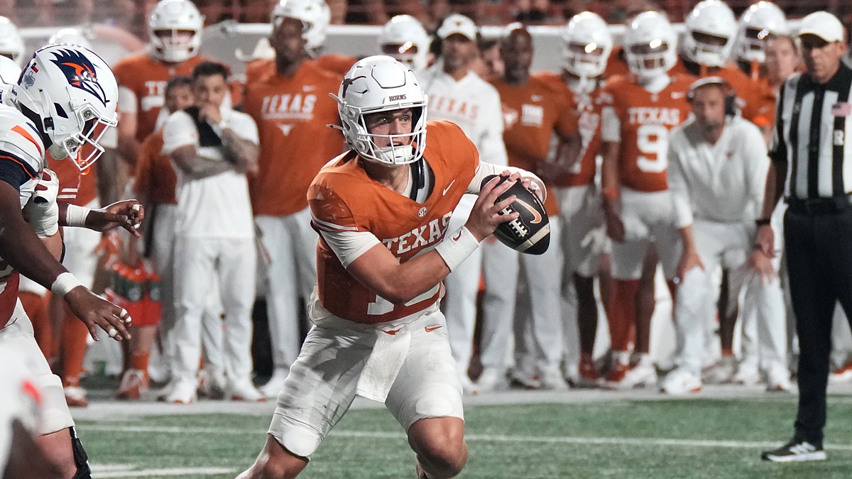 Texas Longhorns quarterback Arch Manning rolls out with the ball in both hands as a UTSA defender closes in.