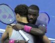 Ben Shelton, back to camera, and Frances Tiafoe hug at the net with their rackets raised after a match.