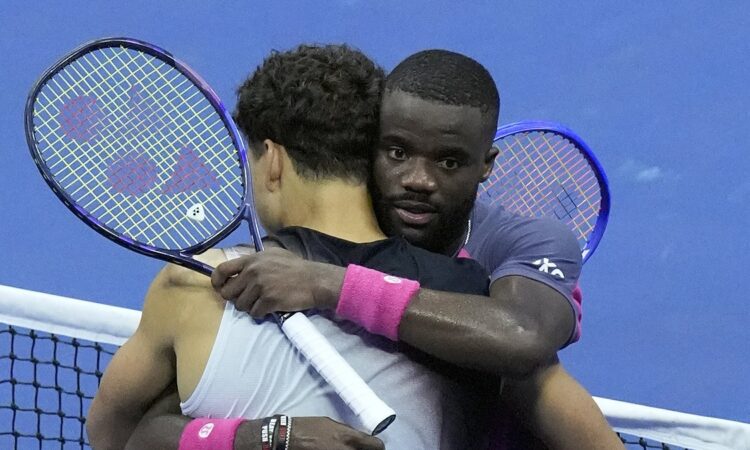 Ben Shelton, back to camera, and Frances Tiafoe hug at the net with their rackets raised after a match.