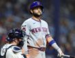 New York Mets third baseman Bo Bichette stands at the plate holding his bat as the Tampa Bay Rays catcher looks away.