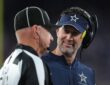 Dallas Cowboys head coach Brian Schottenheimer smiles while speaking with a game official on the sideline.