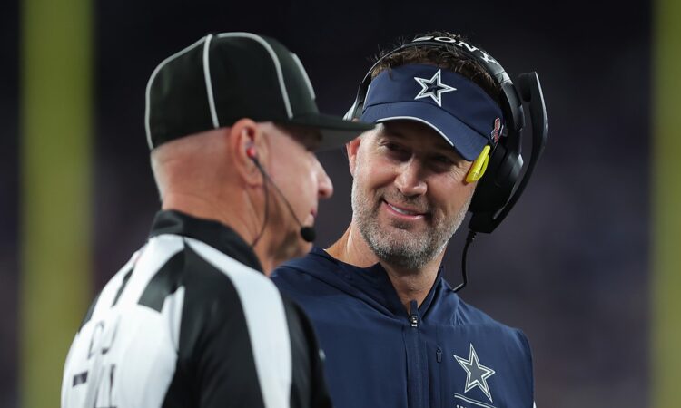 Dallas Cowboys head coach Brian Schottenheimer smiles while speaking with a game official on the sideline.
