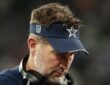 Dallas Cowboys head coach Brian Schottenheimer looks down on the sideline with a headset around his neck.