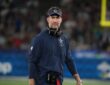 Dallas Cowboys head coach Brian Schottenheimer walks the sideline with a headset around his neck.