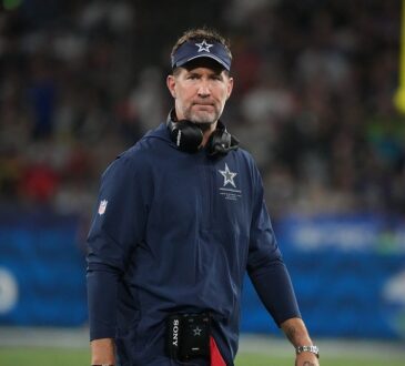 Dallas Cowboys head coach Brian Schottenheimer walks the sideline with a headset around his neck.