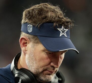 Dallas Cowboys head coach Brian Schottenheimer looks down on the sideline with a headset around his neck.
