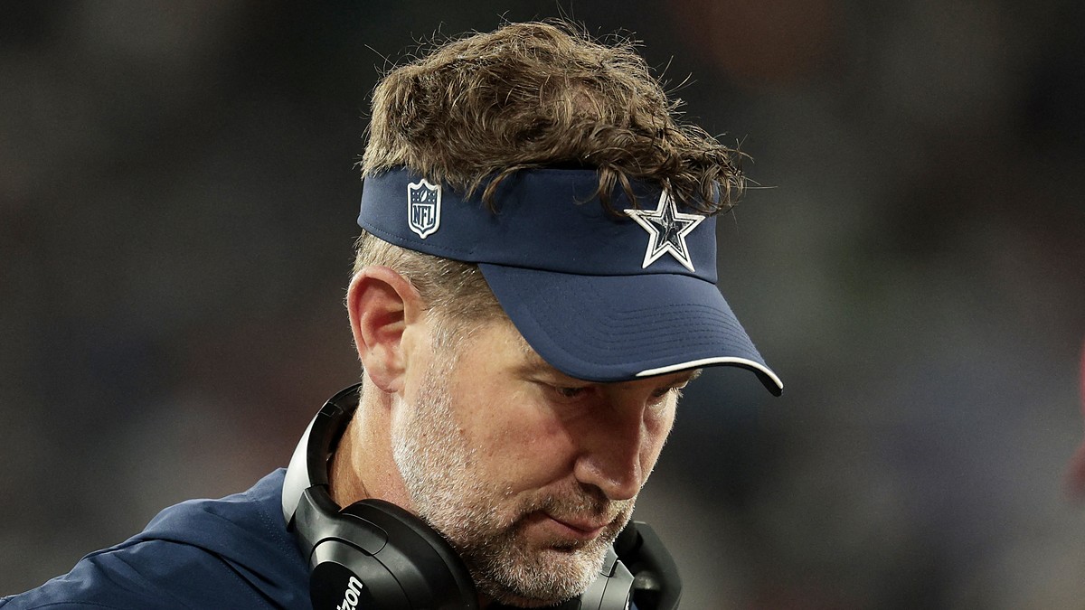 Dallas Cowboys head coach Brian Schottenheimer looks down on the sideline with a headset around his neck.
