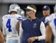 Cowboys head coach Brian Schottenheimer stands among players in warmups and looks toward the field before kickoff.
