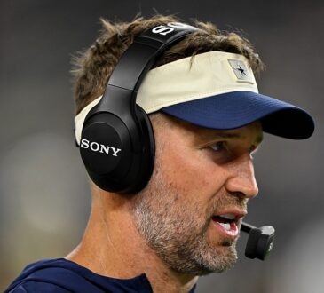 Cowboys head coach Brian Schottenheimer speaks into his headset microphone on the sideline during the game.