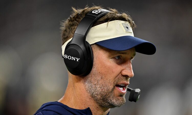 Cowboys head coach Brian Schottenheimer speaks into his headset microphone on the sideline during the game.