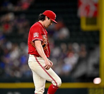 Texas Rangers pitcher Cal Quantrill looks down at his raised leg as he stands on the field in a red Tejas jersey.