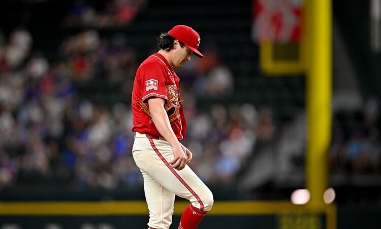 Texas Rangers pitcher Cal Quantrill looks down at his raised leg as he stands on the field in a red Tejas jersey.