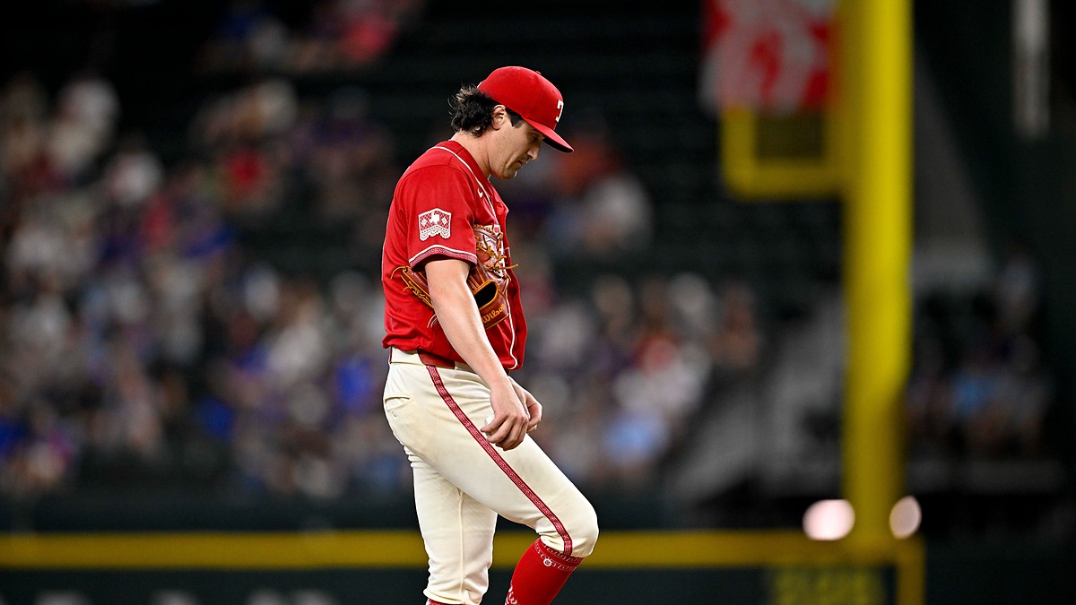 Texas Rangers pitcher Cal Quantrill looks down at his raised leg as he stands on the field in a red Tejas jersey.
