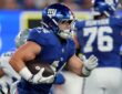 Giants running back Cam Skattebo tucks the ball and cuts upfield with a Cowboys defender trailing behind him.
