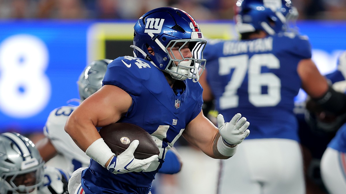 Giants running back Cam Skattebo tucks the ball and cuts upfield with a Cowboys defender trailing behind him.