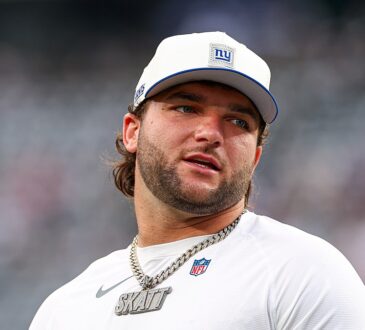 New York Giants running back Cam Skattebo looks toward the sideline in a Giants cap and warmup shirt.