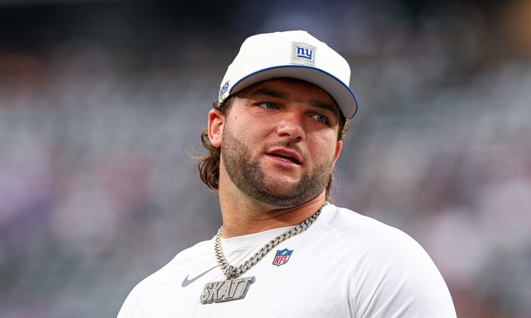 New York Giants running back Cam Skattebo looks toward the sideline in a Giants cap and warmup shirt.