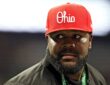 Former Ohio State quarterback Cardale Jones, in a red Ohio cap and a CFP credential lanyard, looks off to his left on the sideline.