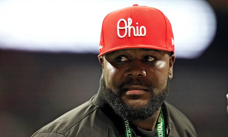 Former Ohio State quarterback Cardale Jones, in a red Ohio cap and a CFP credential lanyard, looks off to his left on the sideline.