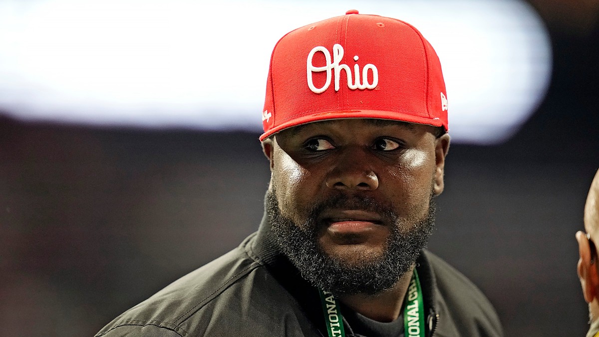 Former Ohio State quarterback Cardale Jones, in a red Ohio cap and a CFP credential lanyard, looks off to his left on the sideline.