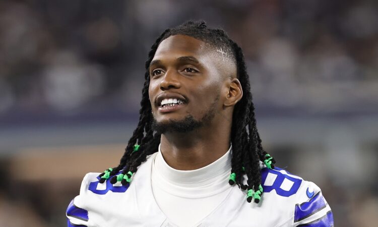 Dallas Cowboys wide receiver CeeDee Lamb smiles as he looks on from the sideline without his helmet.