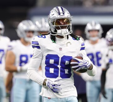 Dallas Cowboys wide receiver CeeDee Lamb holds a football during warmups with teammates behind him.