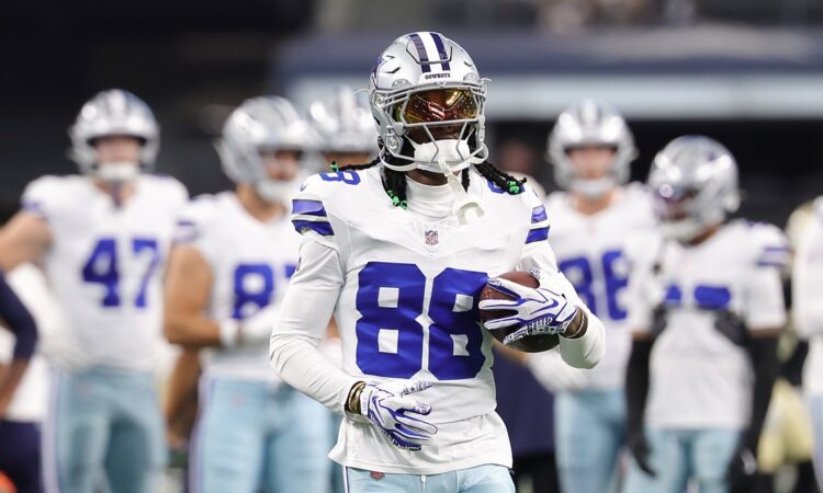 Dallas Cowboys wide receiver CeeDee Lamb holds a football during warmups with teammates behind him.