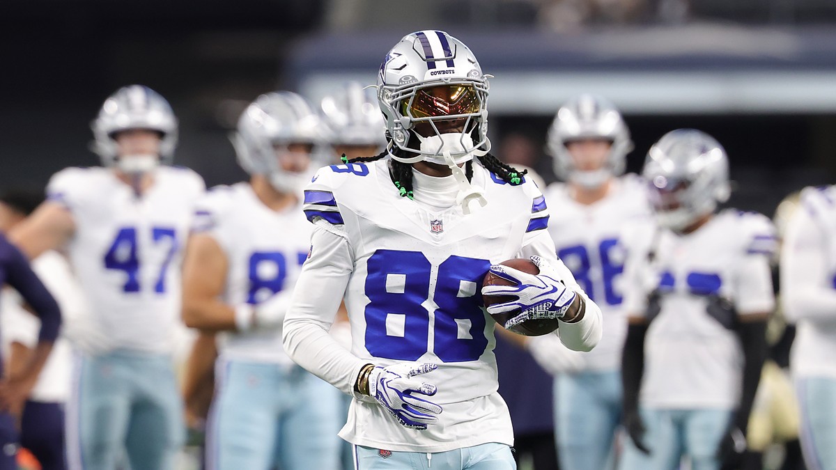 Dallas Cowboys wide receiver CeeDee Lamb holds a football during warmups with teammates behind him.