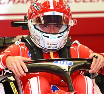 Ferrari driver Charles Leclerc sits in his car gripping the steering wheel with his helmet and visor down.