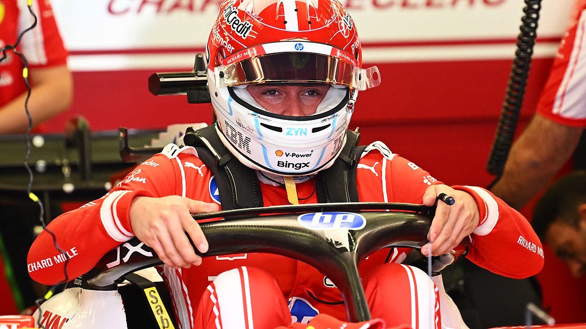 Ferrari driver Charles Leclerc sits in his car gripping the steering wheel with his helmet and visor down.