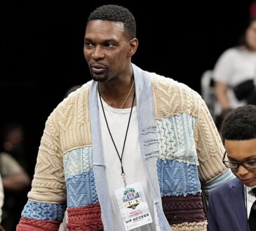 NBA Hall of Famer Chris Bosh, in a patchwork cable-knit cardigan and VIP credential, walks through the courtside crowd.