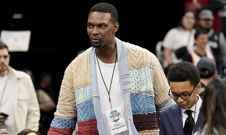 NBA Hall of Famer Chris Bosh, in a patchwork cable-knit cardigan and VIP credential, walks through the courtside crowd.