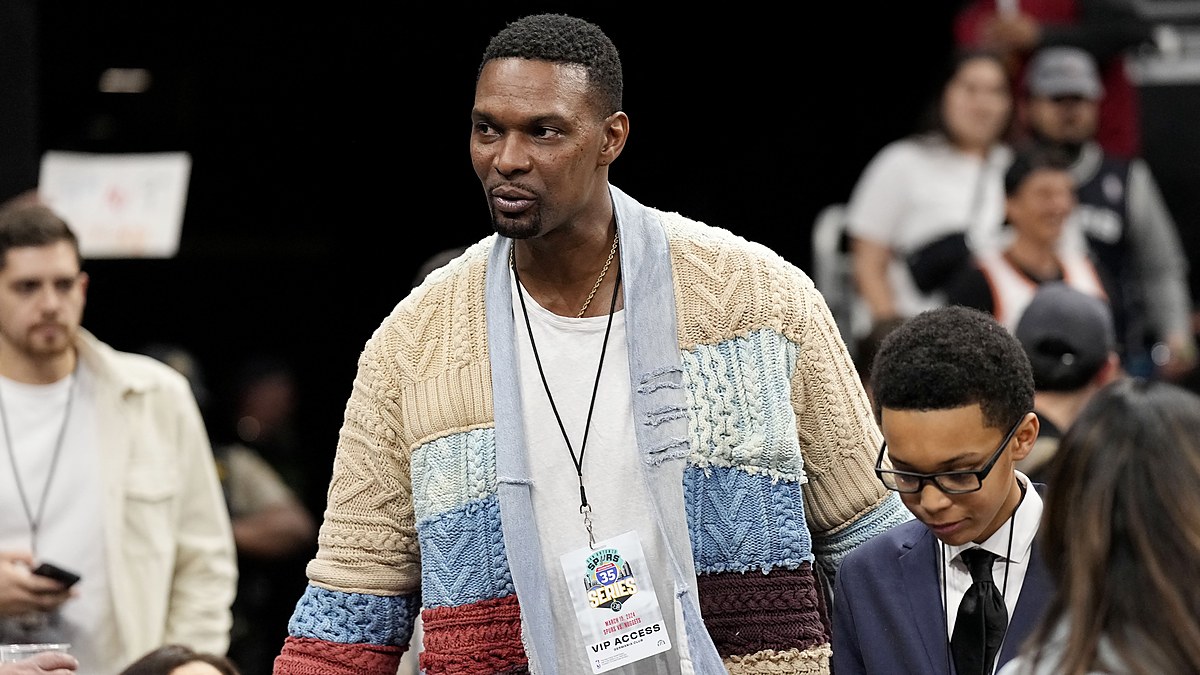 NBA Hall of Famer Chris Bosh, in a patchwork cable-knit cardigan and VIP credential, walks through the courtside crowd.