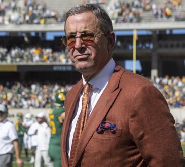 Texas athletics director Chris Del Conte stands on the field in a burnt orange jacket after a game.