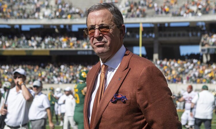 Texas athletics director Chris Del Conte stands on the field in a burnt orange jacket after a game.